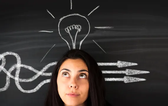 Woman standing in front of a chalkboard with a lightbulb above her head