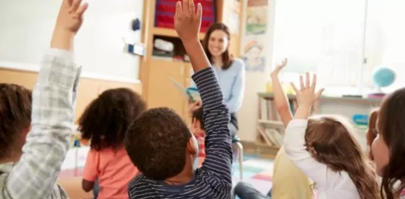 Elementary school kids raising hands to teacher