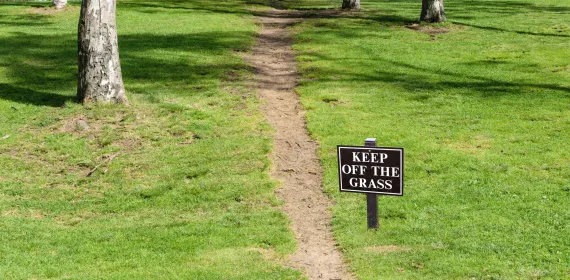 A dirt path with a sign Keep Off the Grass