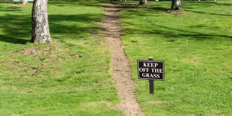 A dirt path with a sign Keep Off the Grass